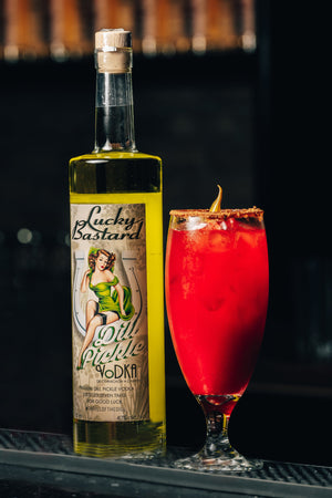Bottle of 'Lucky Bastard Dill Pickle Vodka' with a red caesar cocktail on a bar counter