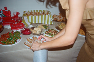 Person reaching for a plate of food on a table with various dishes and snacks.