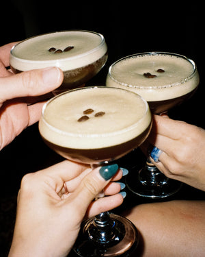 Three hands toasting with cocktails against a dark background