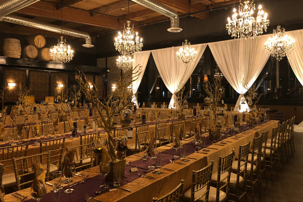 Light white and gold photo of Lucky Bastard Distillers with wooden floors and high ceilings, set up for an event with chairs and tables. 1920 style prohibition era Bar and event room decorated for a wedding in Saskatoon Saskatchewan YXE Canada must see must do while visiting bridge city.