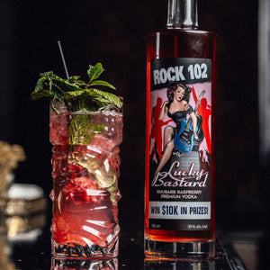 Bottle of Rock 102 Lucky Bastard Vodka with a mojito cocktail garnished with mint leaves on a dark background