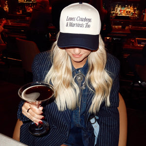 Person in a bar wearing a cap with text and holding a espresso martini cocktail.