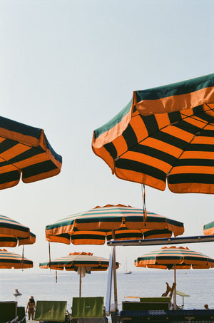 Orange and Blue Striped beach umbrellas with a clear sky and ocean background