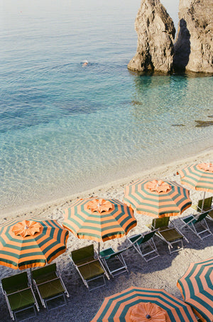 Beach scene with colorful Orange & Blue umbrellas and chairs near a rocky coastline.