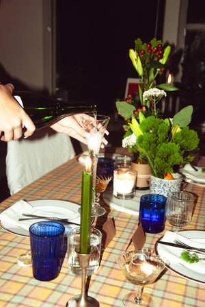 Dining table set with blue glasses, candles, and a floral arrangement.