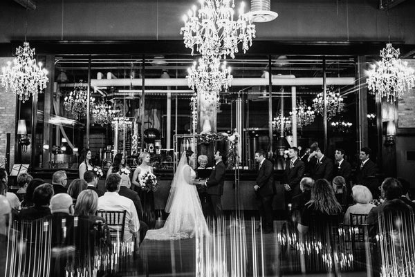 Wedding ceremony taking place in a grand hall with chandeliers. Lucky Bastard Distillers with wooden floors and high ceilings, set up for an event with chairs and tables. 1920 style prohibition era Bar and event room decorated for a wedding in Saskatoon Saskatchewan YXE Canada must see must do while visiting bridge city.