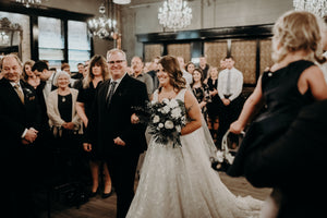 Wedding ceremony with a bride walking down the aisle, surrounded by guests. Lucky Bastard Distillers with wooden floors and high ceilings, set up for an event with chairs and tables. 1920 style prohibition era Bar and event room decorated for a wedding in Saskatoon Saskatchewan YXE Canada must see must do while visiting bridge city.