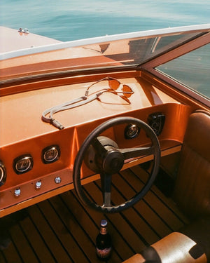 Orange boat interior with steering wheel and dashboard, featuring sunglasses and a bottle.